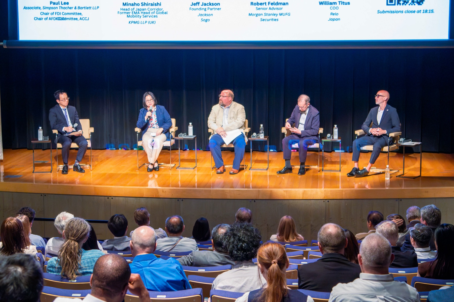 Four panellists seated on stage in front of a full audience at a chamber event